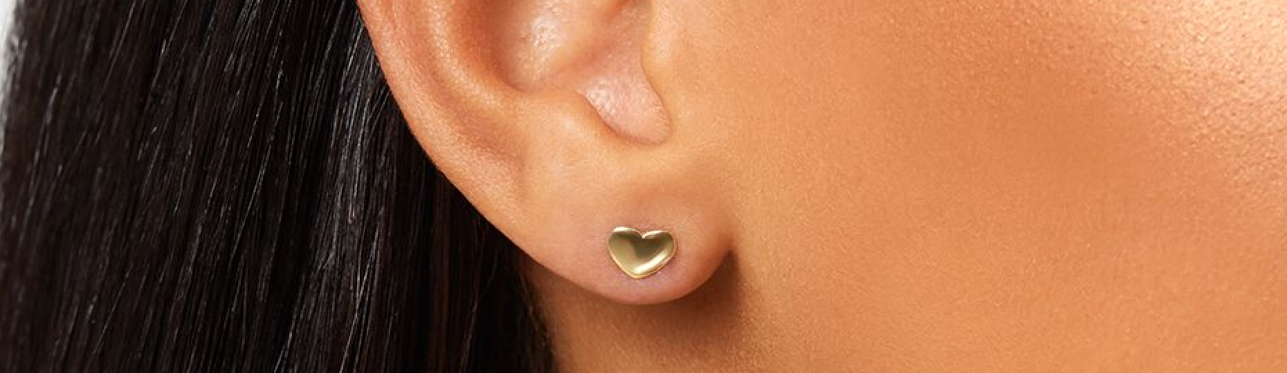 Gold heart stud earrings in womans earlobe