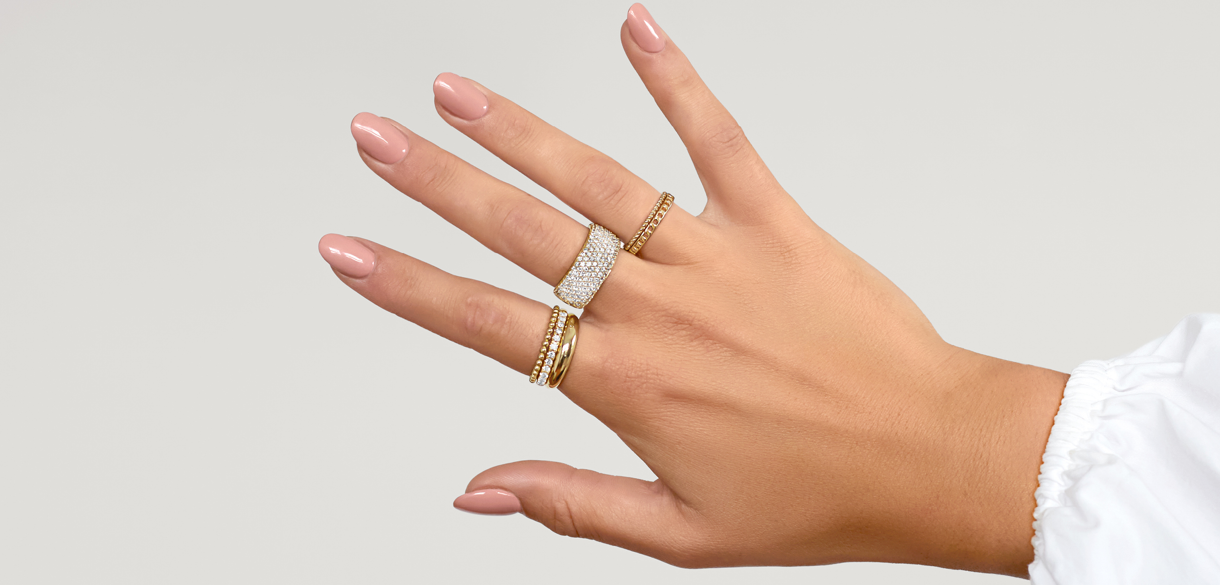 Female hand with multiple rings stacked together, including a statement diamond ring, diamond dainty rings and plain yellow gold bands.