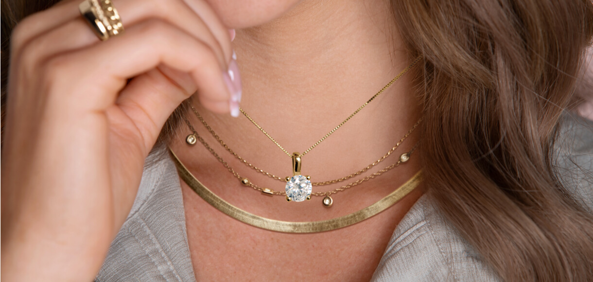 Diamond solitaire necklace stacked on other gold necklaces