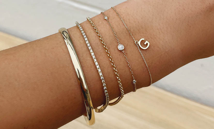 Five yellow gold bracelets stacked on a wrist