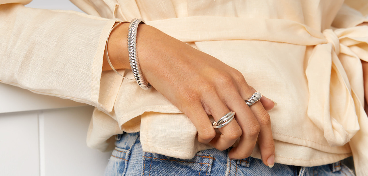 female hand wearing two 925 sterling silver rings and two bangles