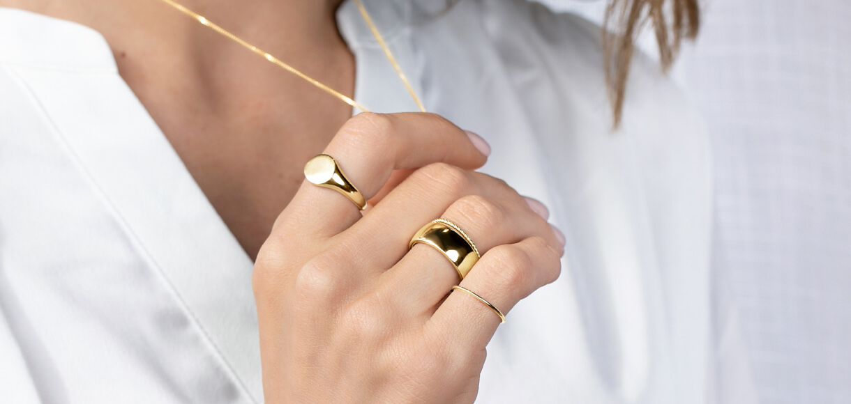 Gold jewellery on model featuring signet ring, stacker ring, necklace and curved ring