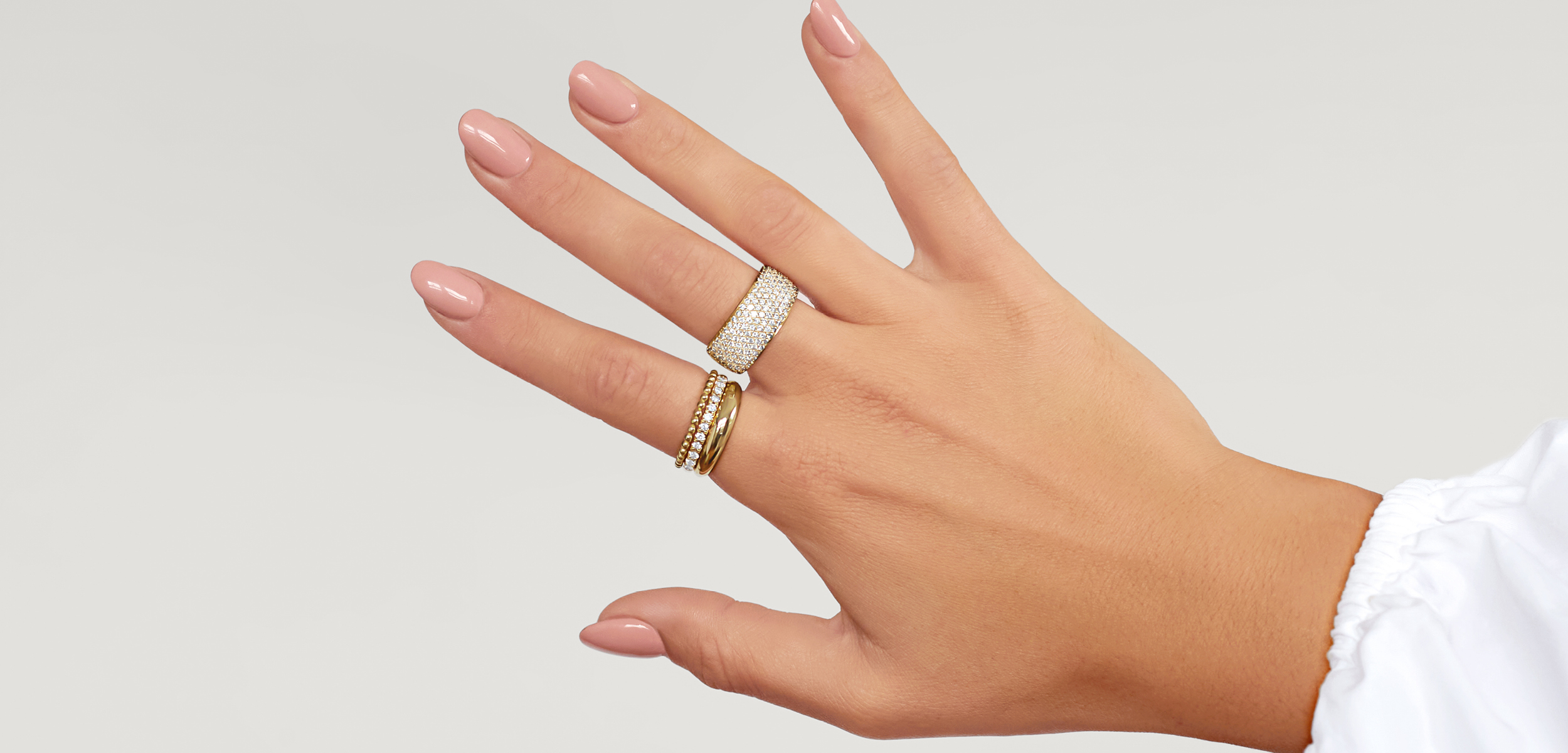 Female hand with statement diamond ring, a narrow diamond ring and more dainty diamond rings, all stacked together.