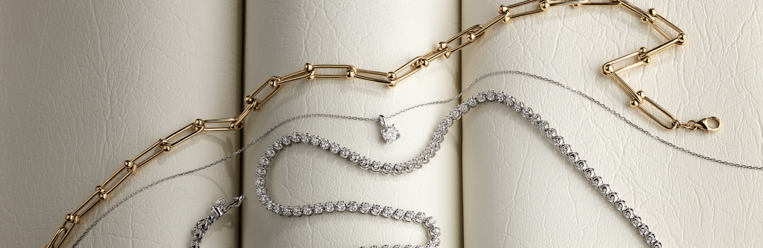 Flat lay of gold chain, diamond pendant and tennis necklace 