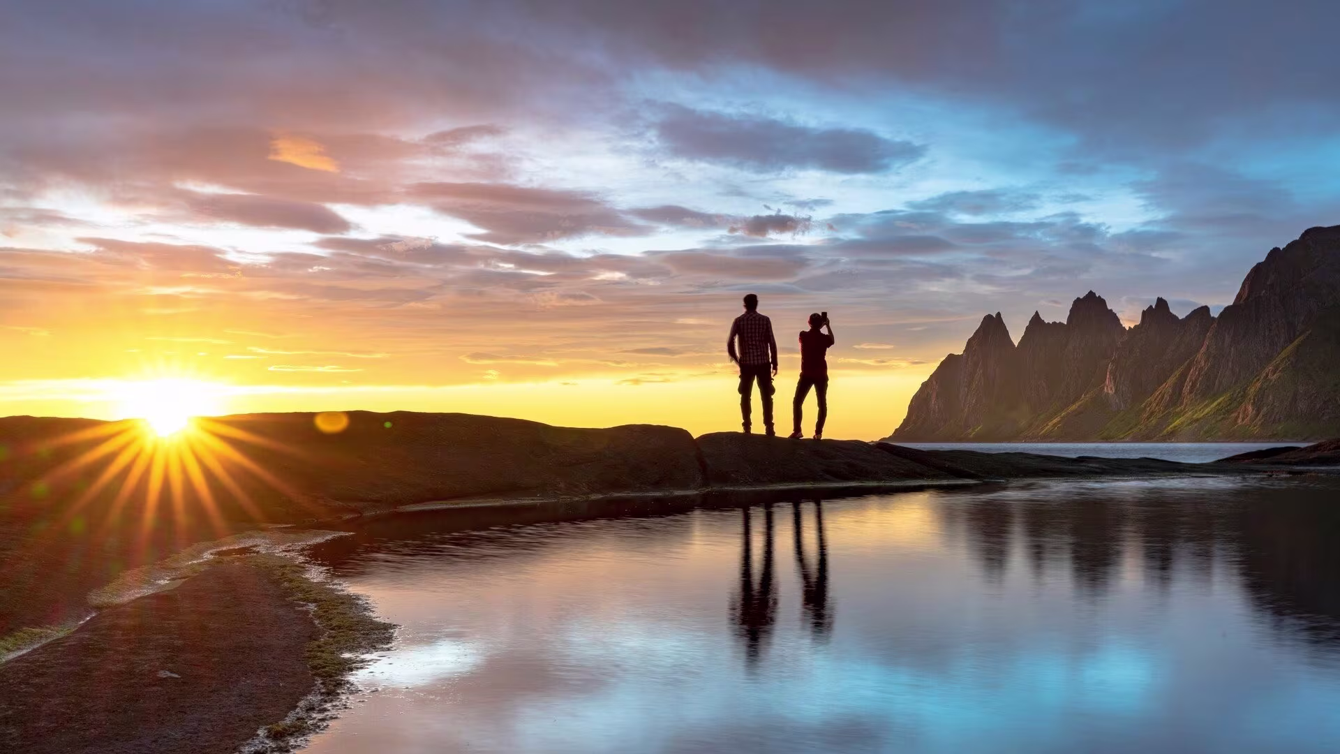 Couple watching a golden sunset over the fjords in Senja, Norway