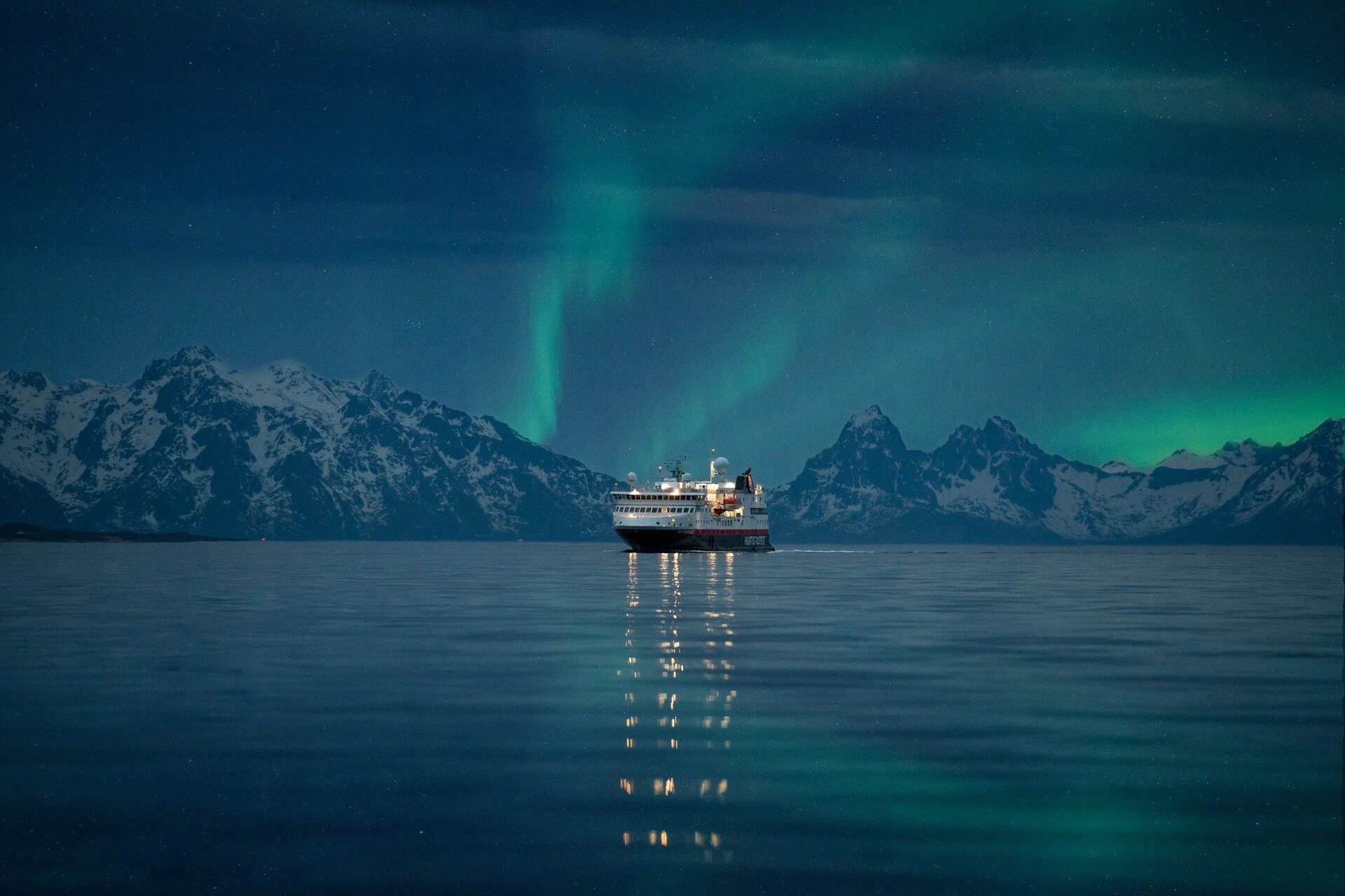 A Hurtigruten ship sailing in Norway with the Northern Lights above