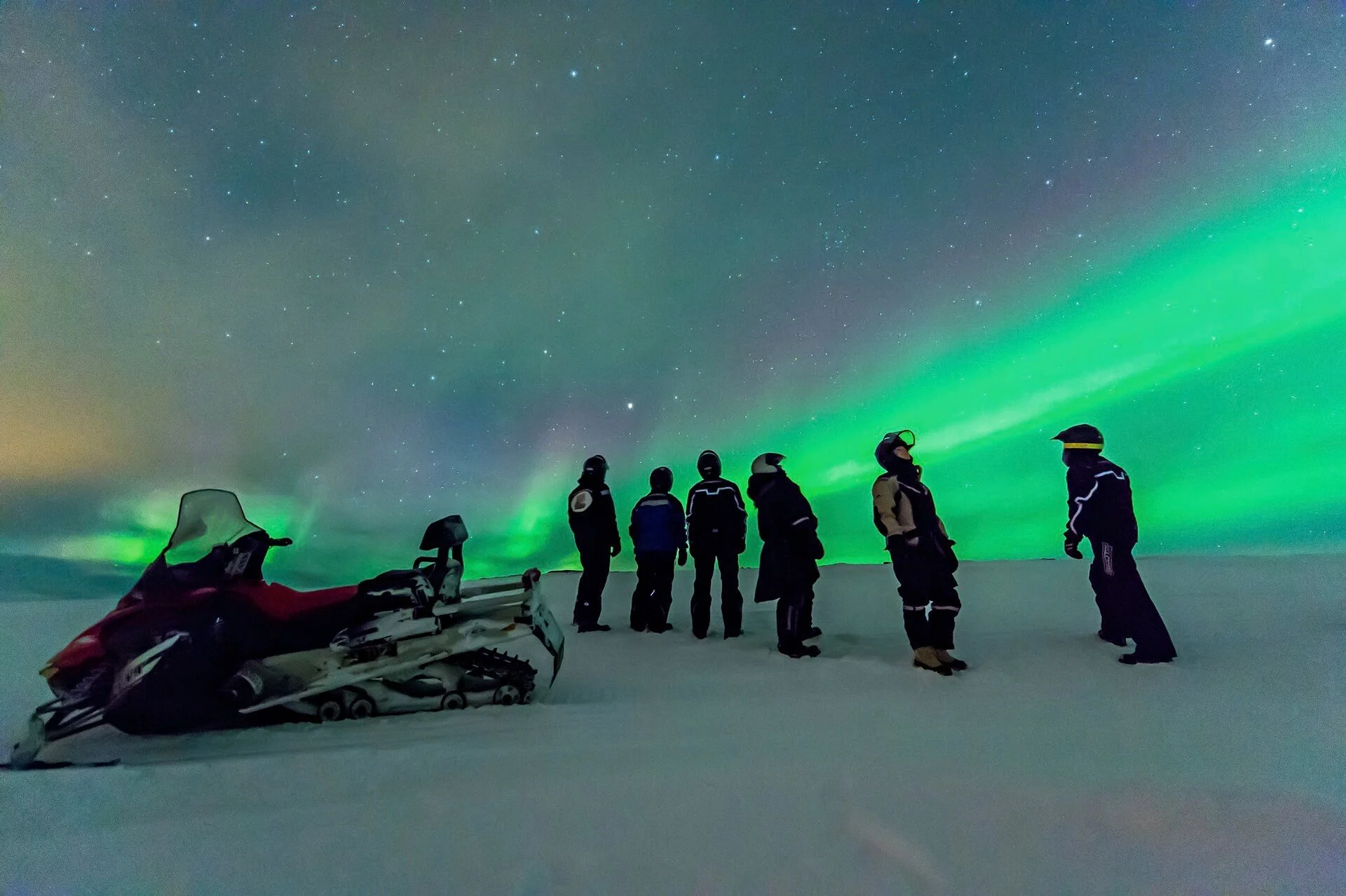 A group of tourists on a snowmobile excursion in Norway under the Northern Lights