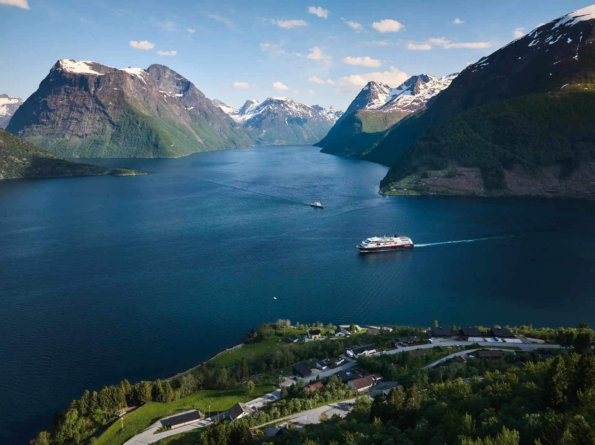 MS Trollfjord sailing through Hjorundfjorden with snow capped mountains in the background