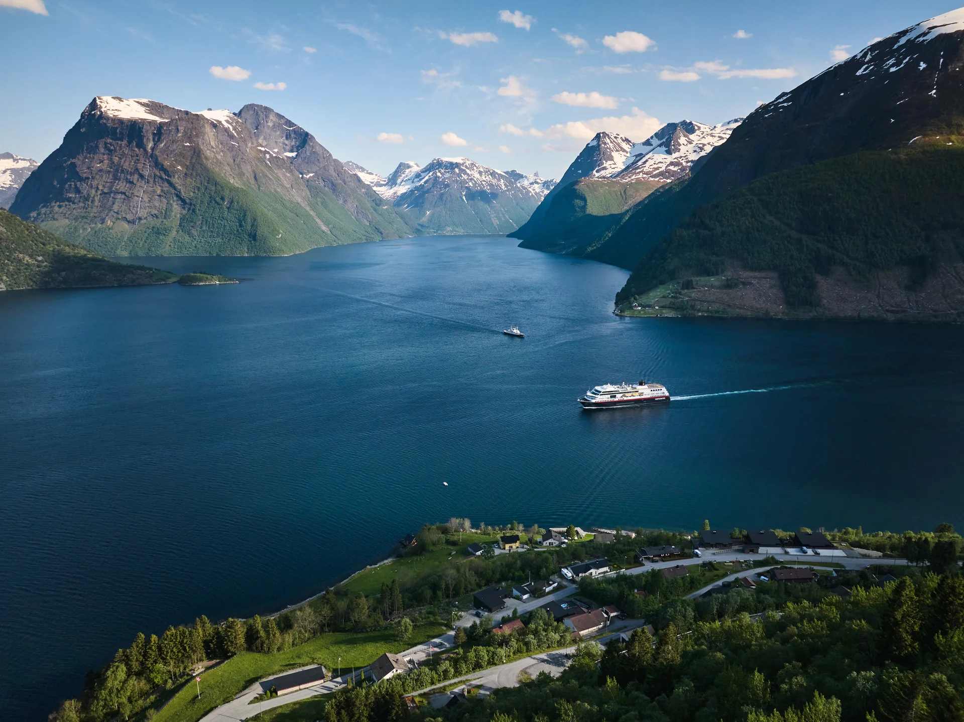 MS Trollfjord sailing through Hjorundfjorden with snow capped mountains in the background