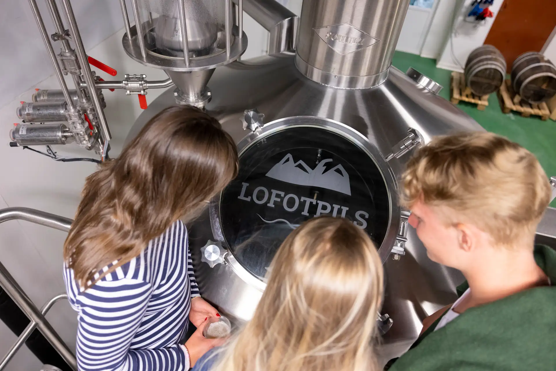 Drei Besucher blicken bei einer Führung durch die Brauerei Lofotpils in Svolvær auf den Lofoten in einen grossen Braukessel aus Edelstahl hinab.