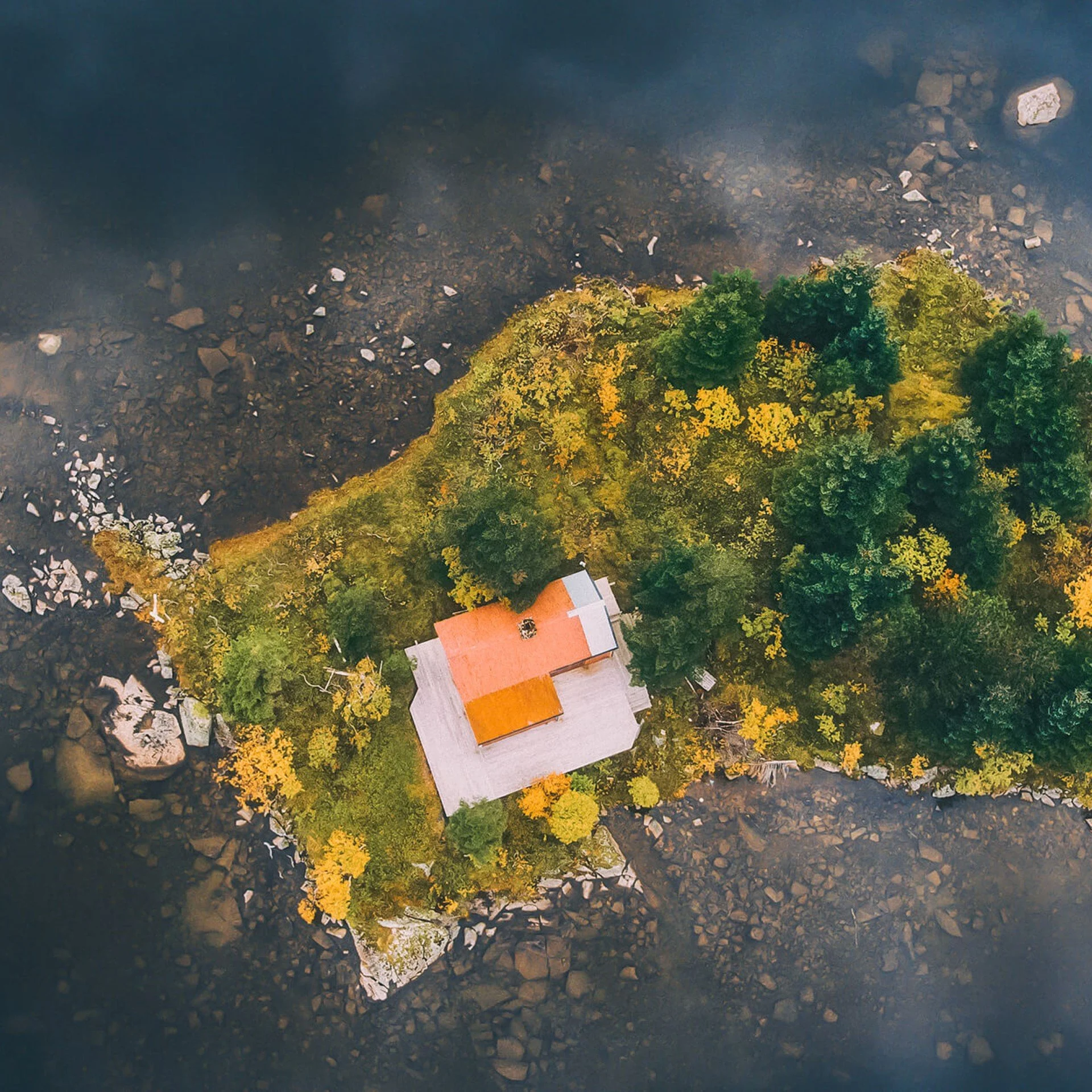 Island seen from above, a drone photo. Lots of trees and one house with orange roof