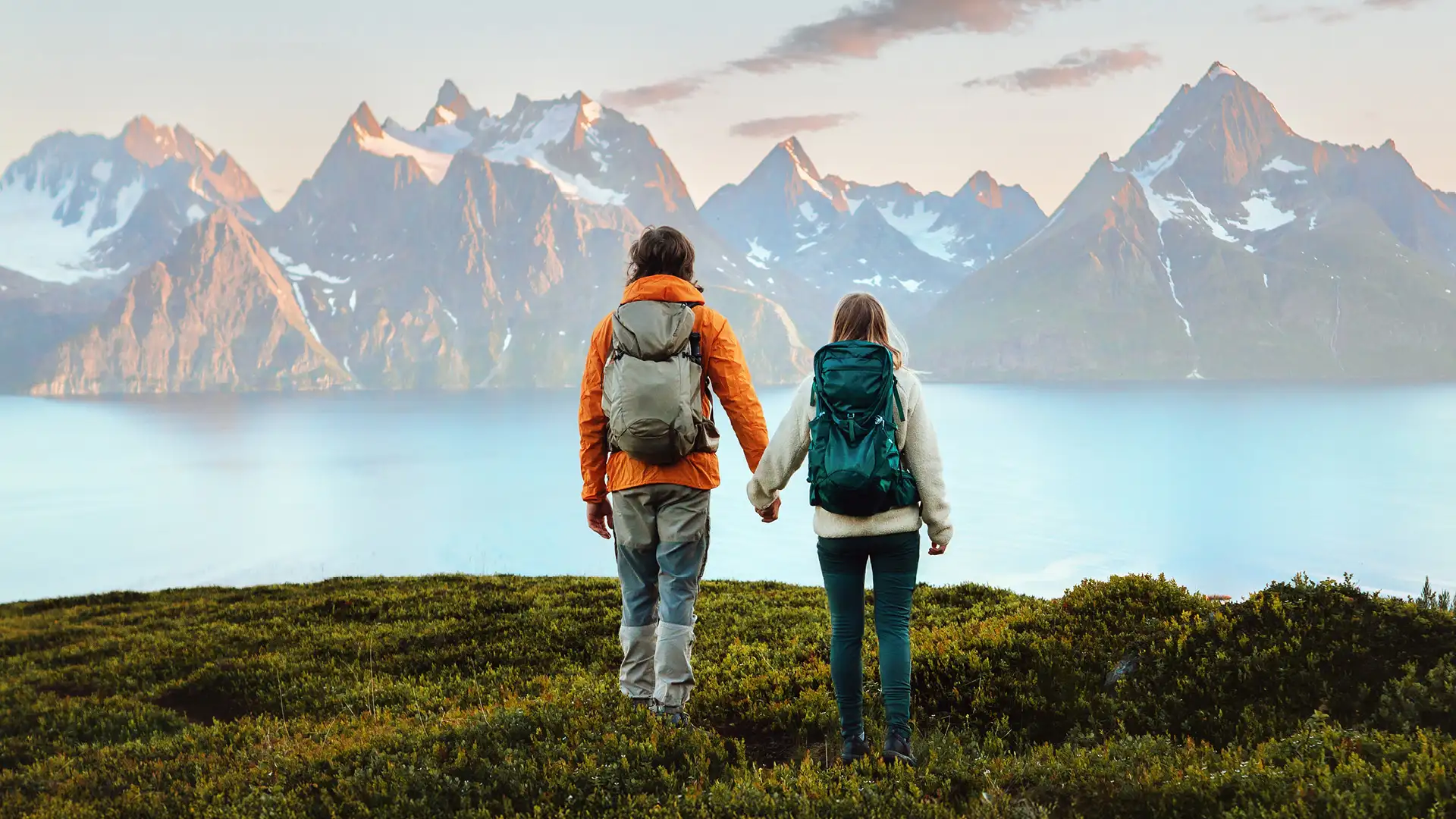 Two people standing on hill looking at oceans and mountains