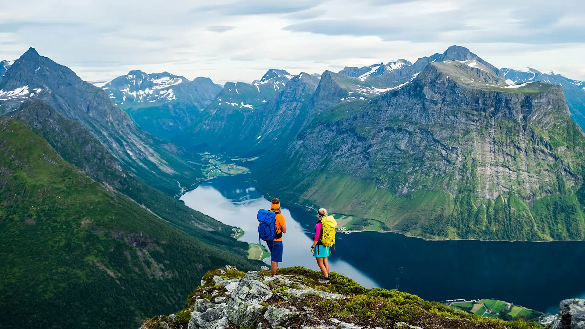 Two people standing on hill looking at oceans and mountains