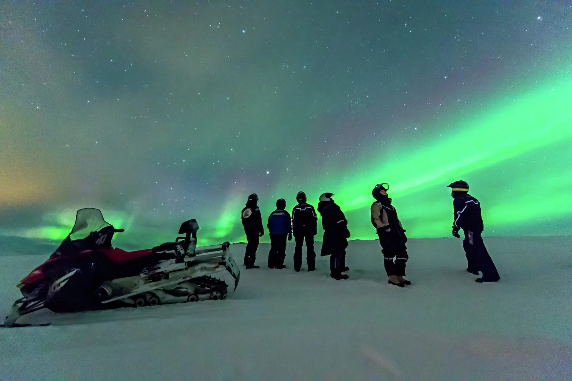 Un groupe de touristes en motoneige sous les aurores boréales en Norvège.