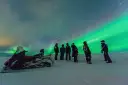 A group of tourists on a snowmobile trip underneath the Northern Lights in Norway