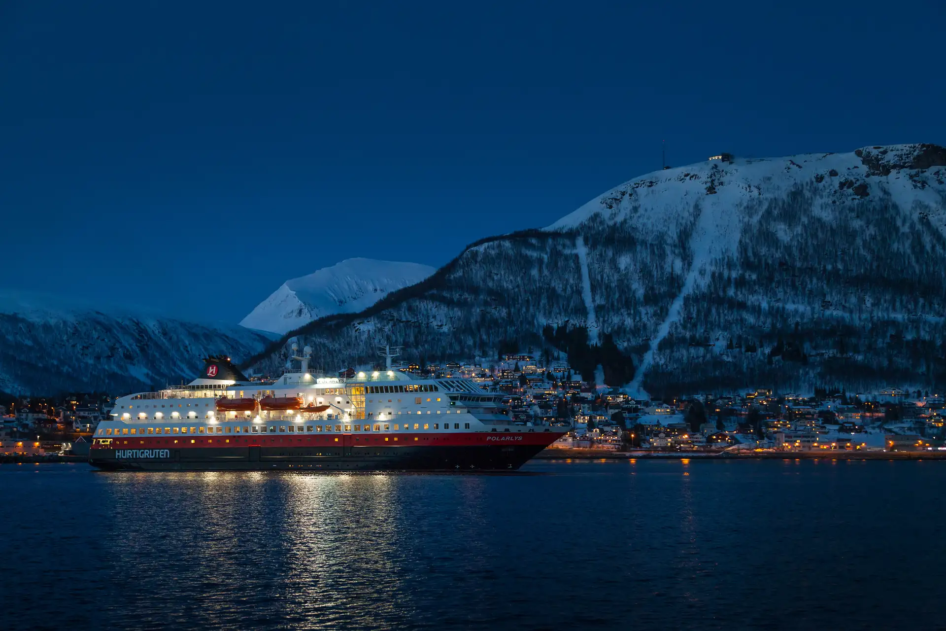 MS Polarlys sailing past Tromsø, which is covered in snow and lights