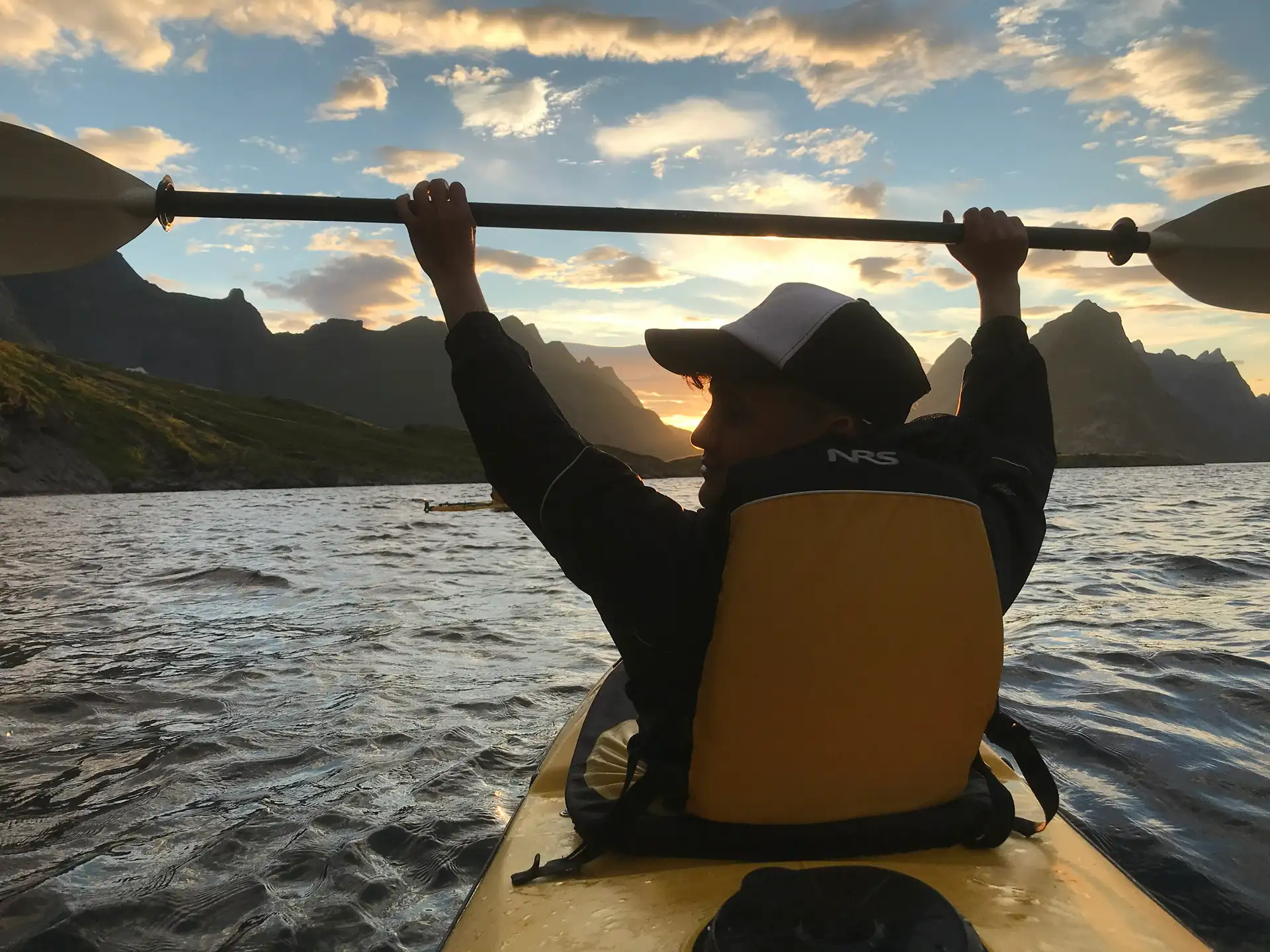 person-holding-paddle-above-head-kayak-water-reine-lofoten