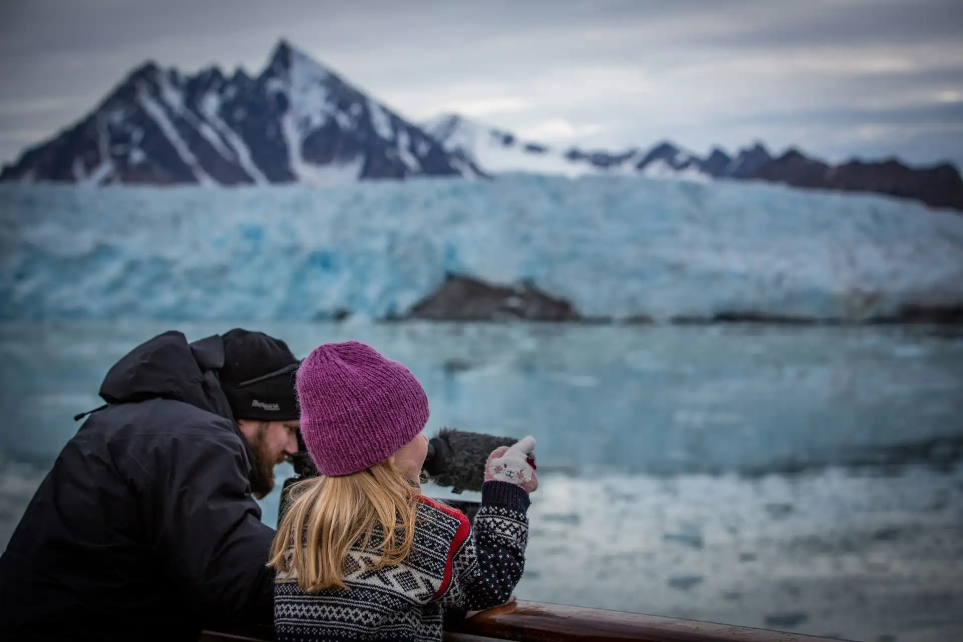 Two people staning on deck and taking photos of the breathtaking mpuntains and glaicers in the background.