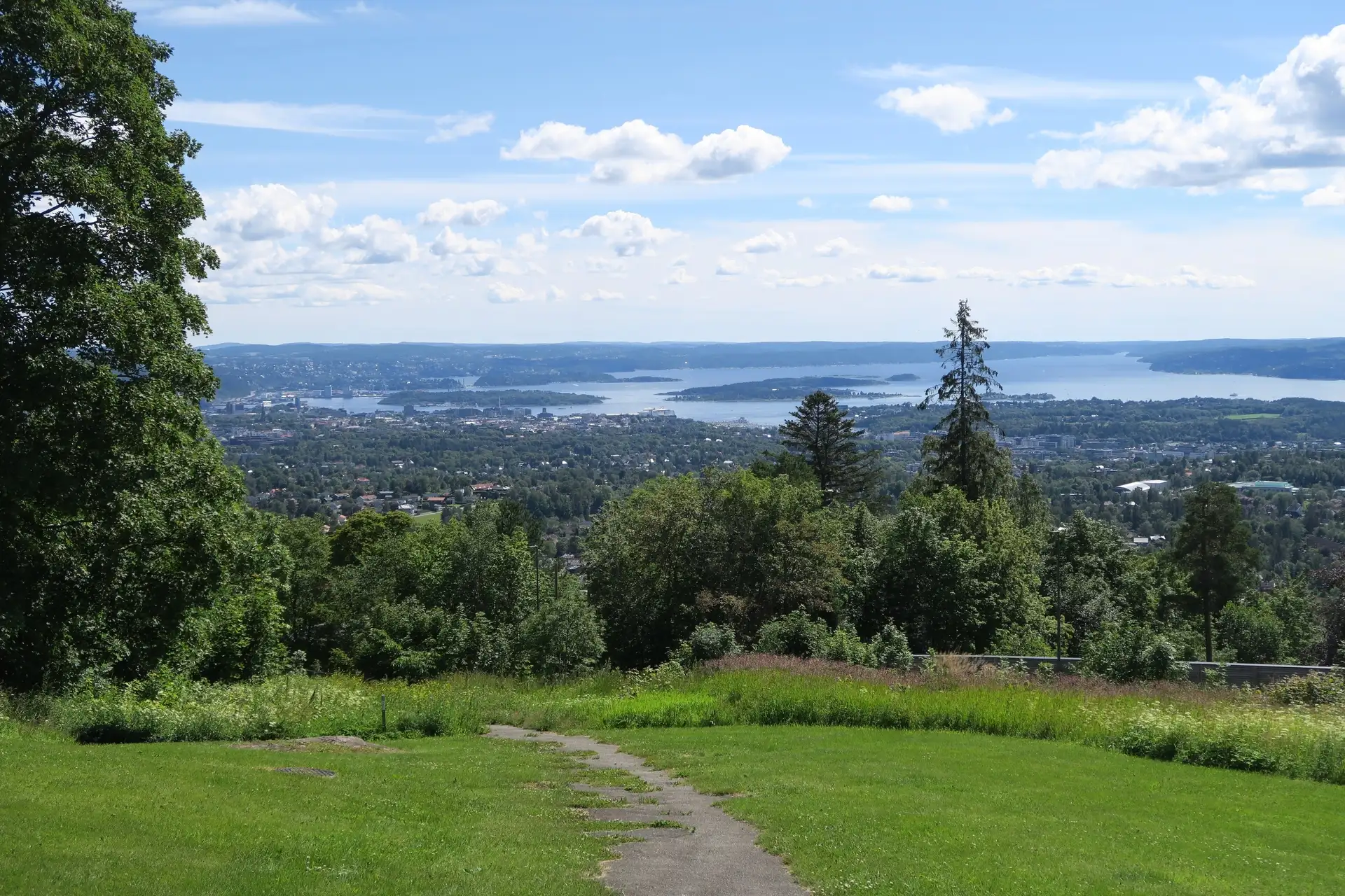 Panoramic summer view over Oslo and the Oslofjord from the wooded hillside of Holmenkollen, with the city and its islands stretching toward the horizon