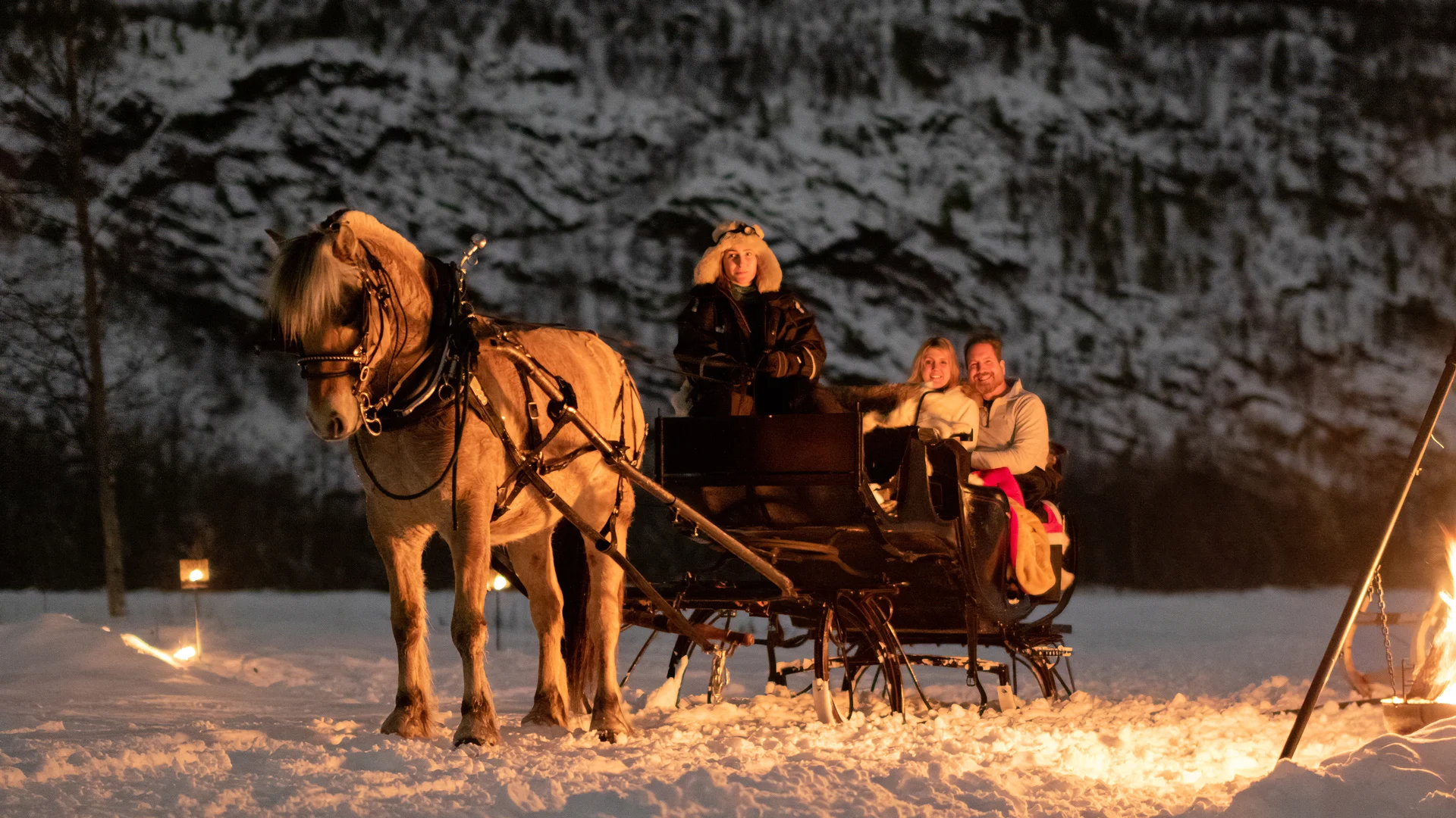Eine von Pferden gezogene Kutsche im Schnee neben einem Feuer in Norwegen.