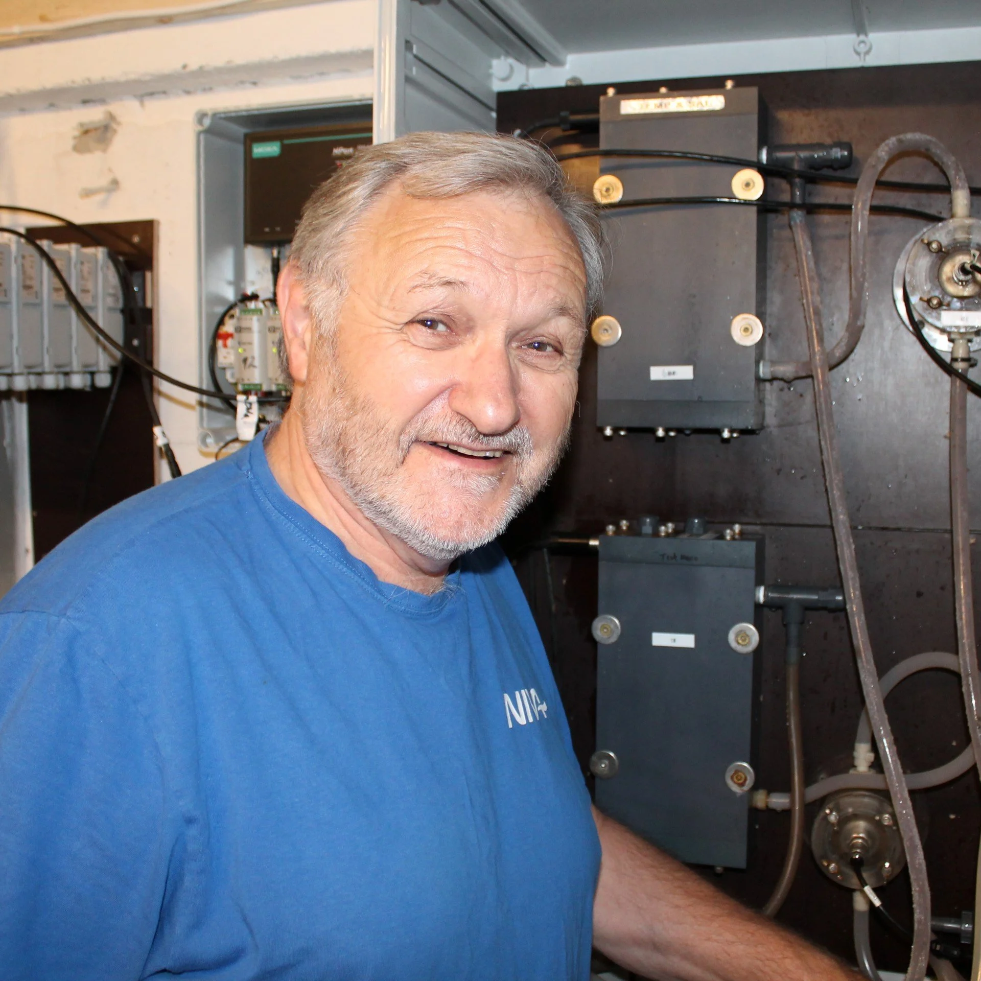 Kai Sørensen is standing in the engine room. He is wearing a blue shirt, and he is smiling.