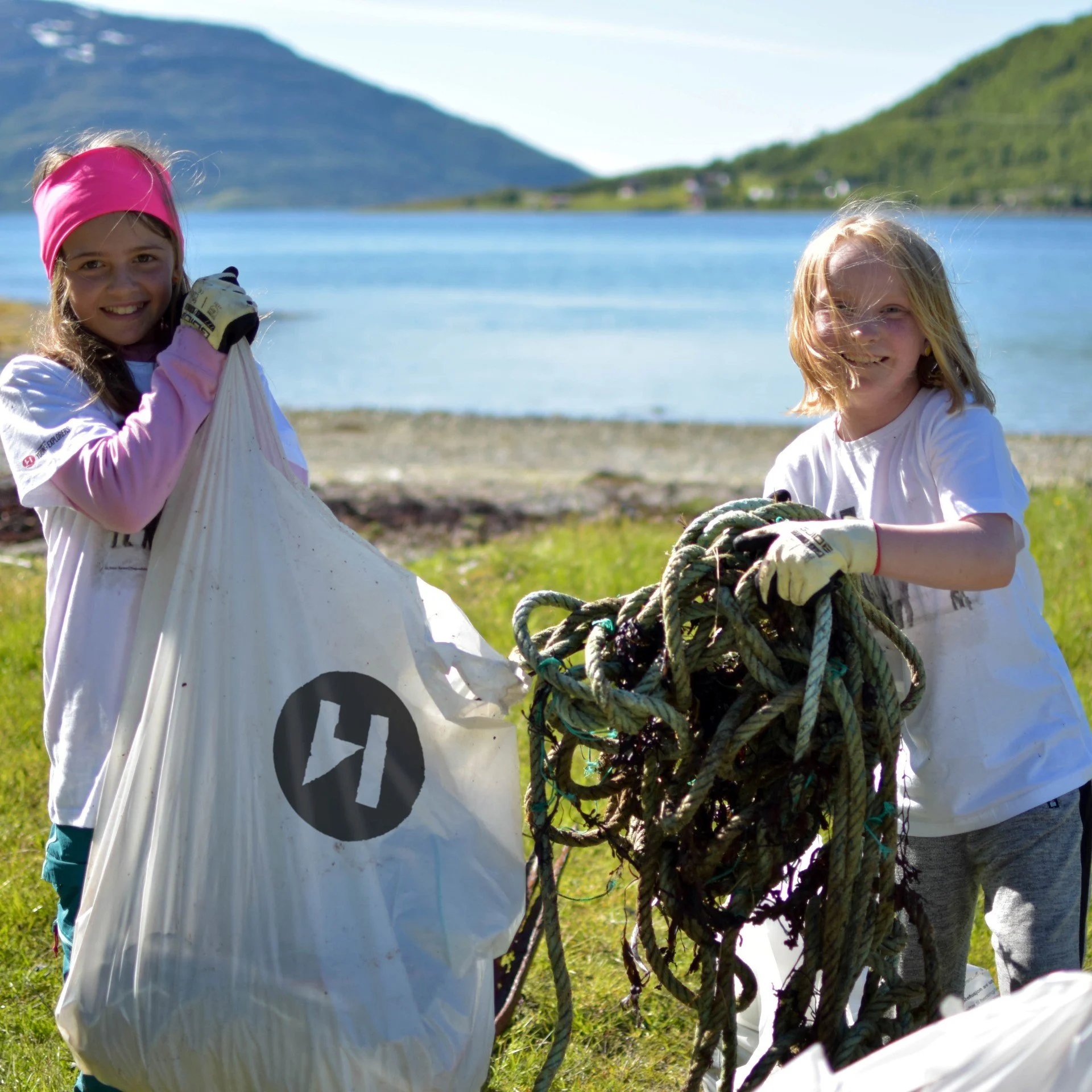Two young girls, young explorers, cleaning the beach. Both are carrying loads of old ropes and trash found