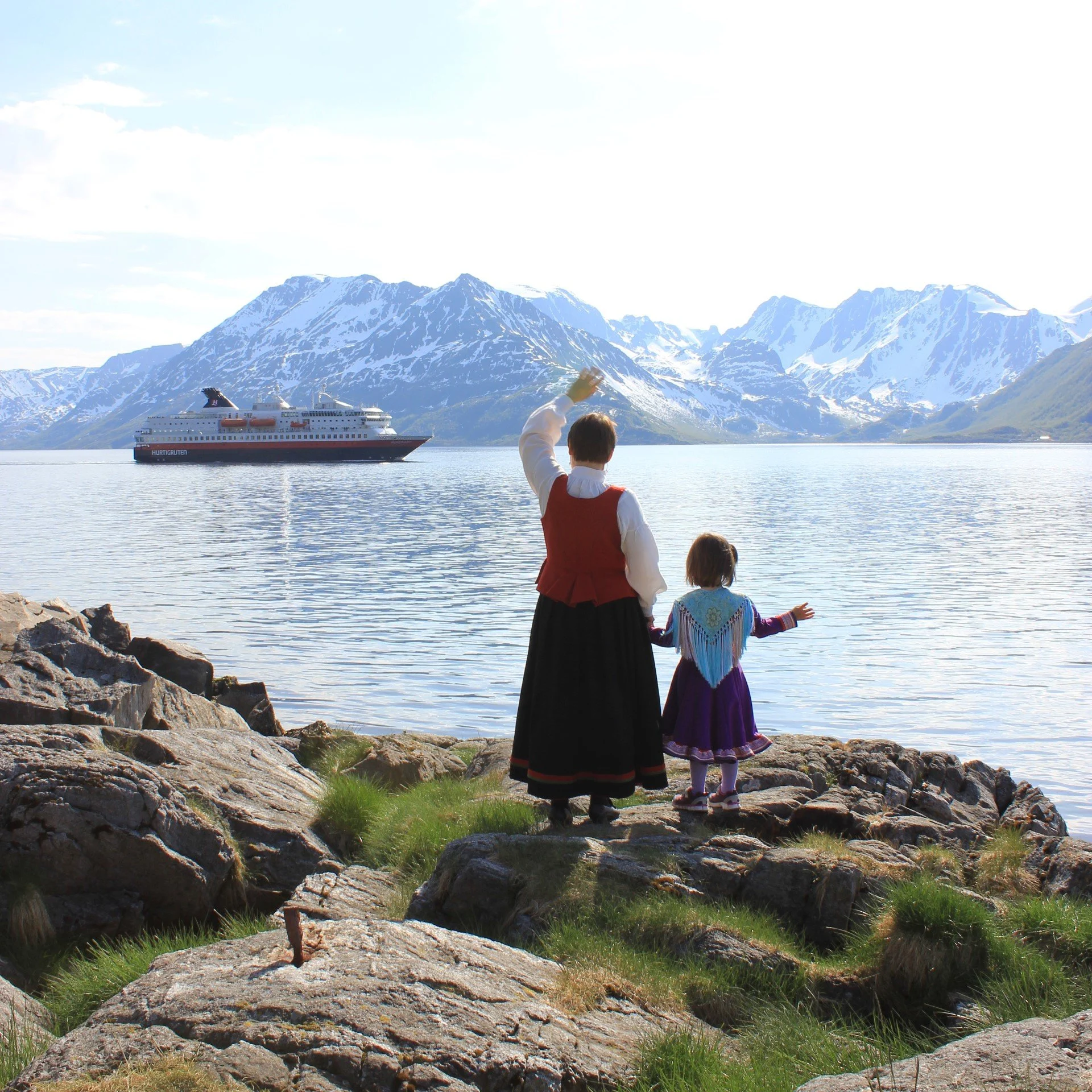 Two generations waving to a Hurtigruten ship as it sails by