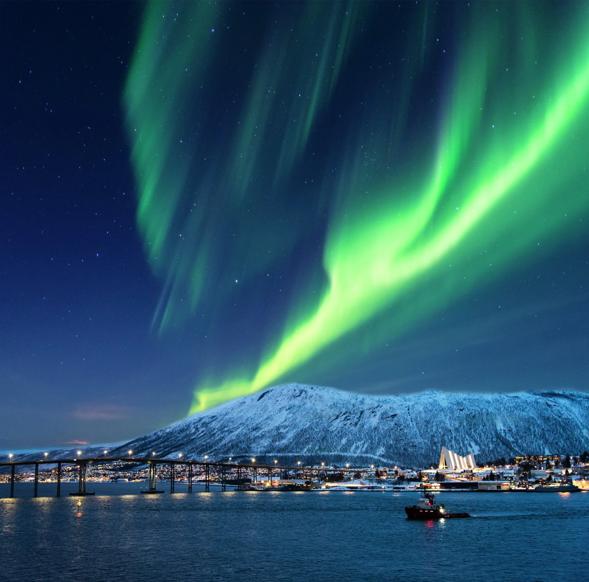 Beautiful Northern Lights dancing on the sky above the city of Tromsø and the Arctic Cathedral, Norway.