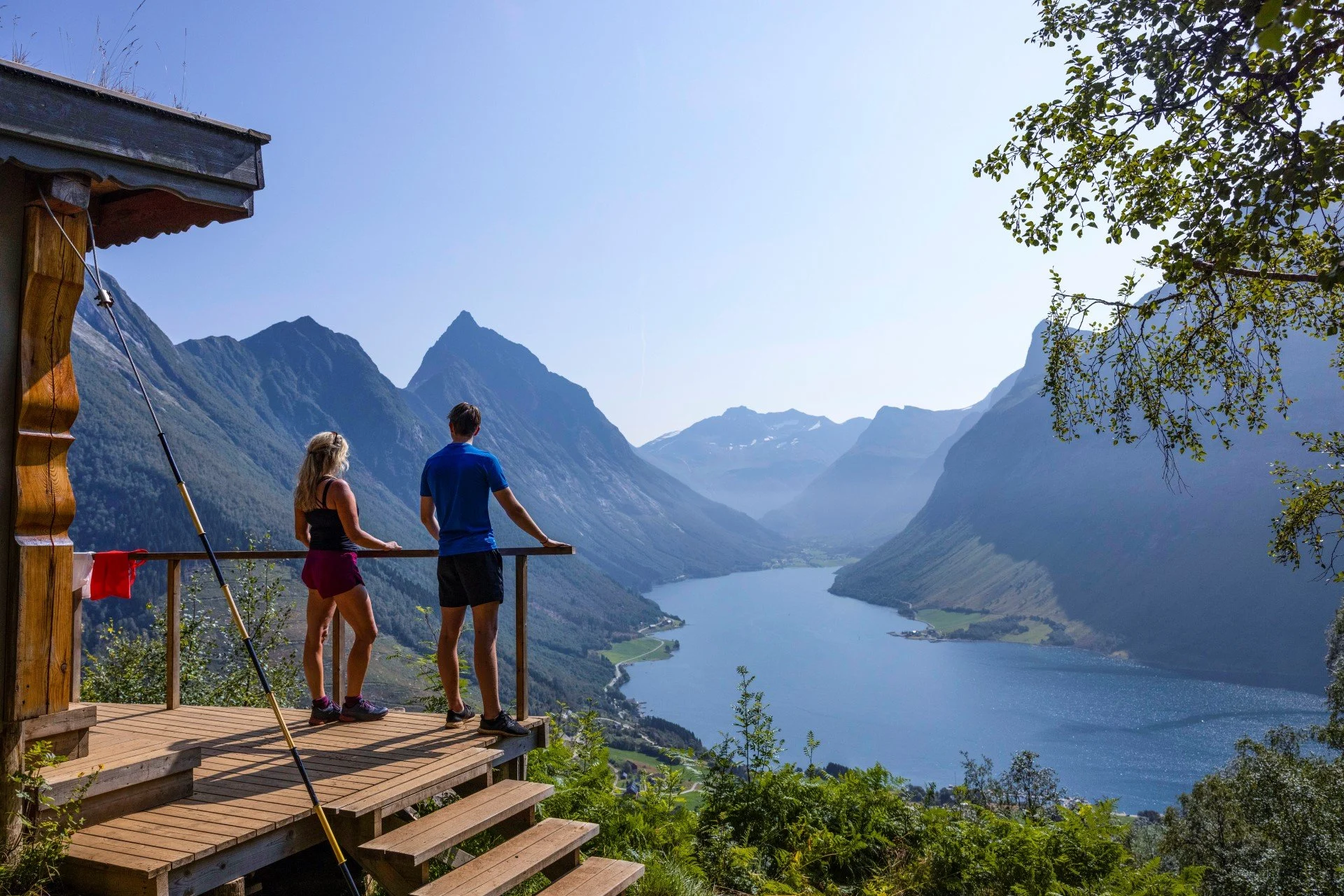 A couple is standing on a viewpoint overlooking Hjørundfjorden. Vestcoast, Norway