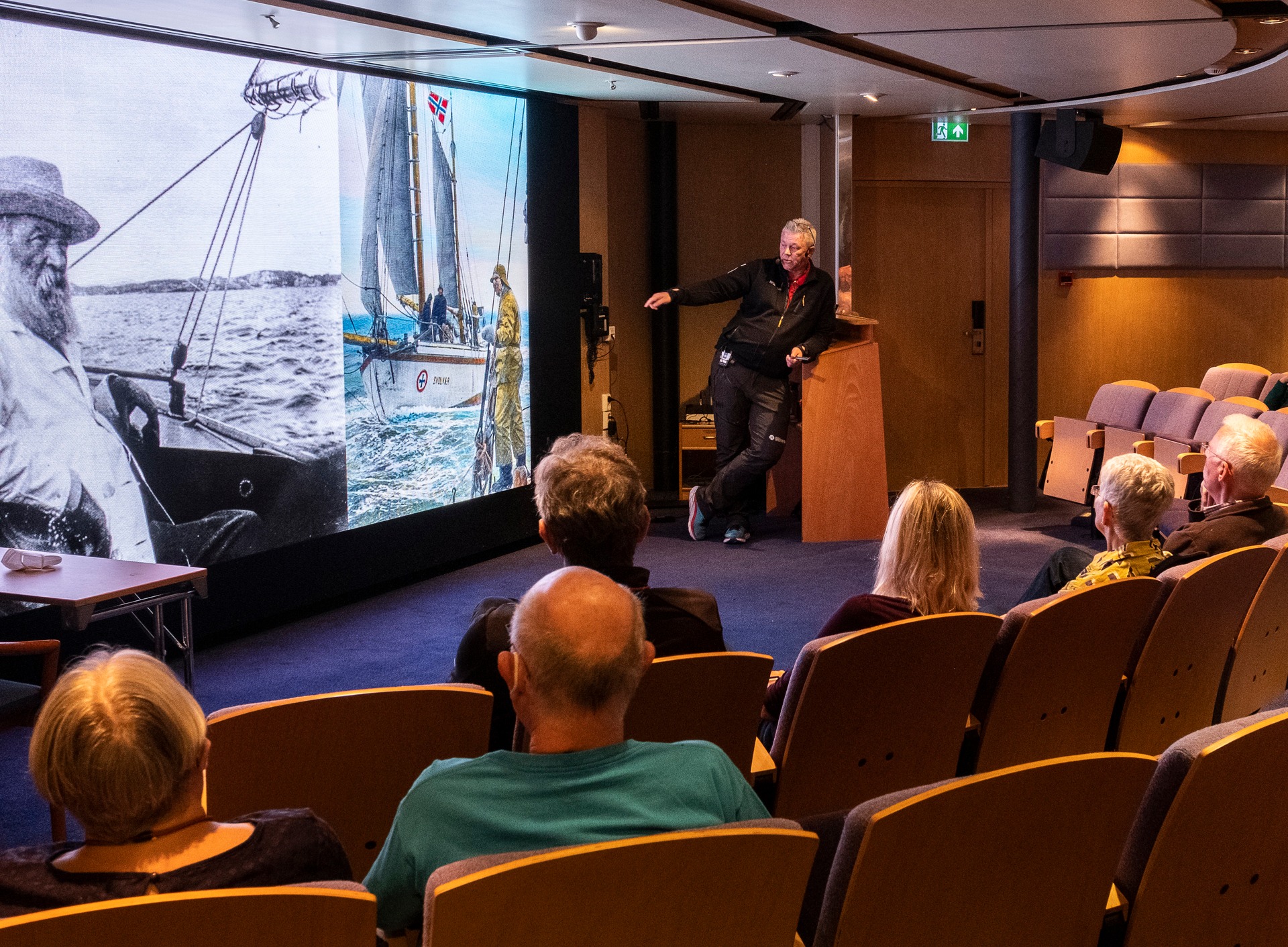 Lecturer speaking in front of seated audience using slide about Norway