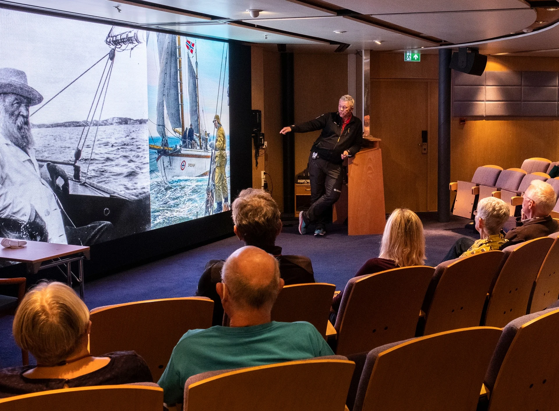 Lecturer speaking in front of seated audience using slide about Norway