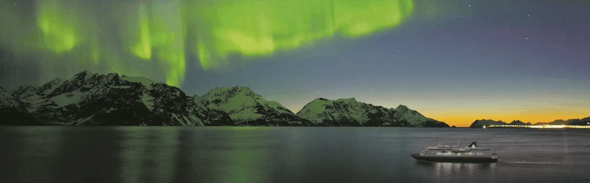 Green northern lights over Lyngsalpene mountains above a Hurtigruten ship at in Norway