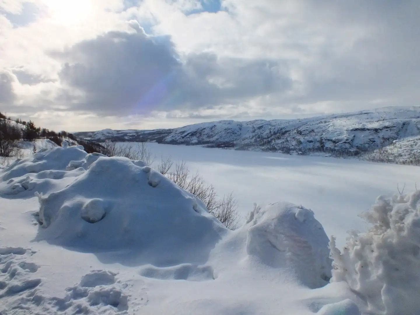 Snow-covered rocks and a frozen lake surrounded by bare Arctic tundra and snow-dusted hills near Kirkenes, Finnmark, Northern Norway