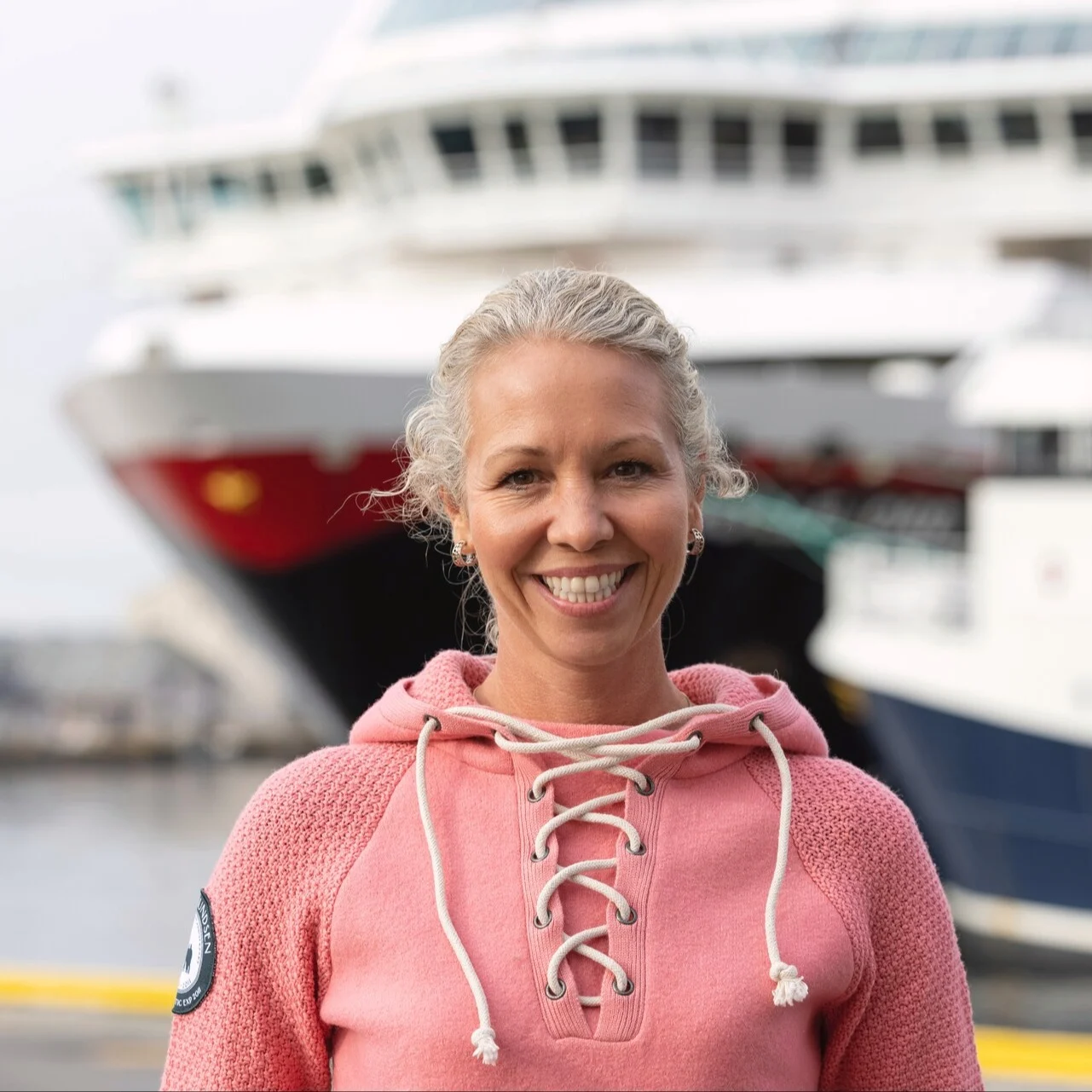 Hedda Felin, Hurtigruten Norway CEO is standing in front of a Hurtigruten ship on the Norwegian Coast