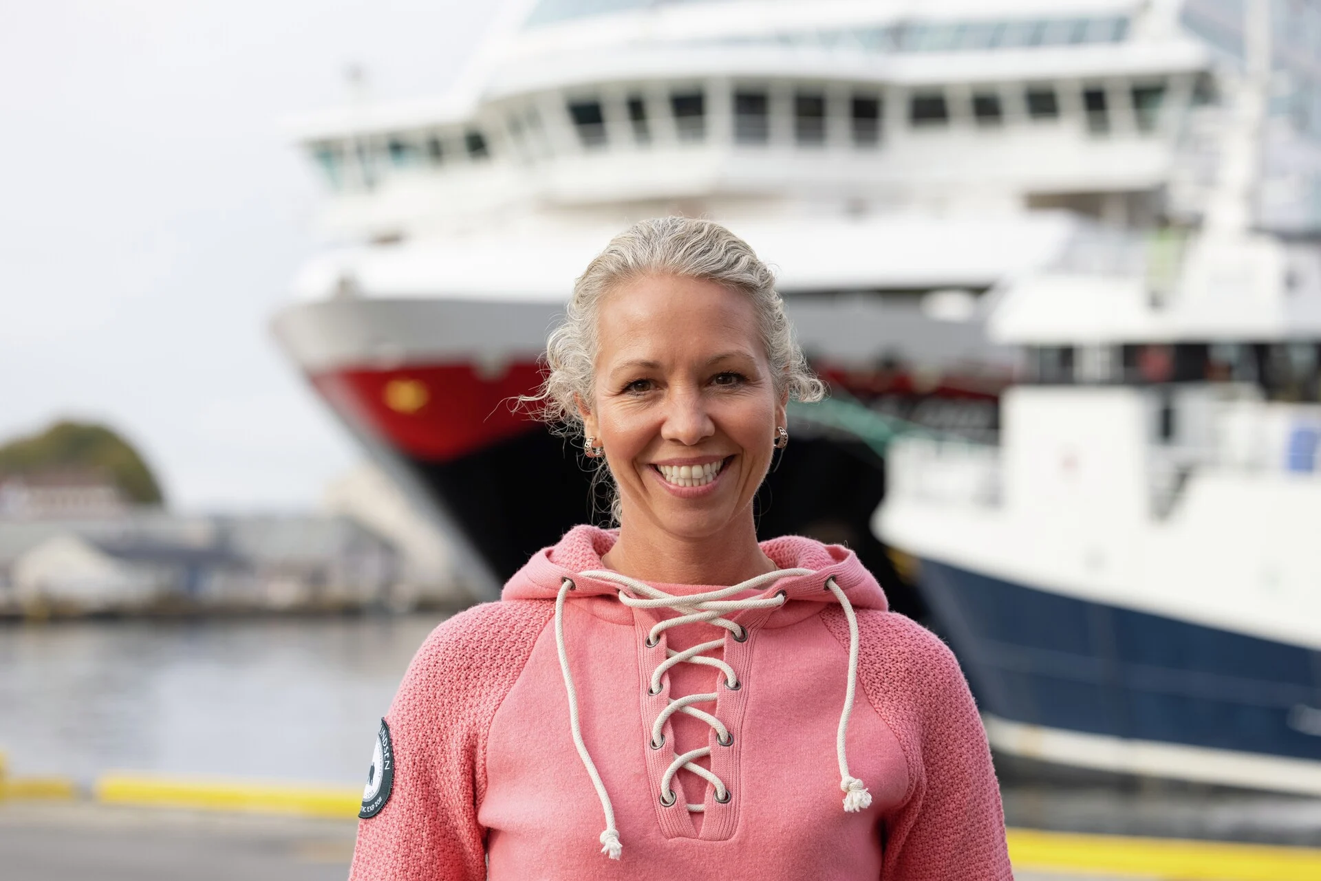 Hedda Felin, Hurtigruten Norway CEO is standing in front of a Hurtigruten ship on the Norwegian Coast