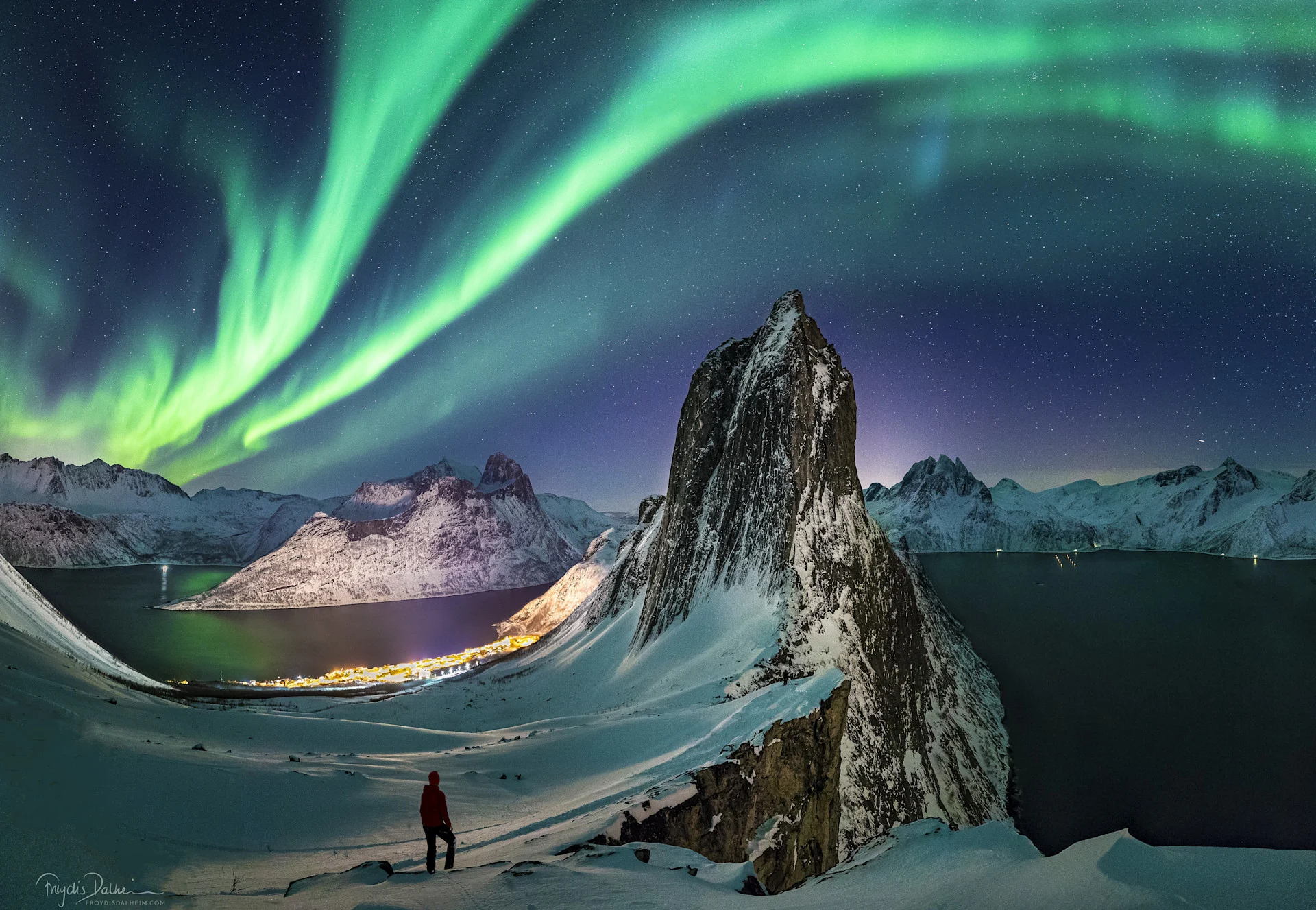 Man walking along Senja fjords at night under vibrant green northern lights in Norway