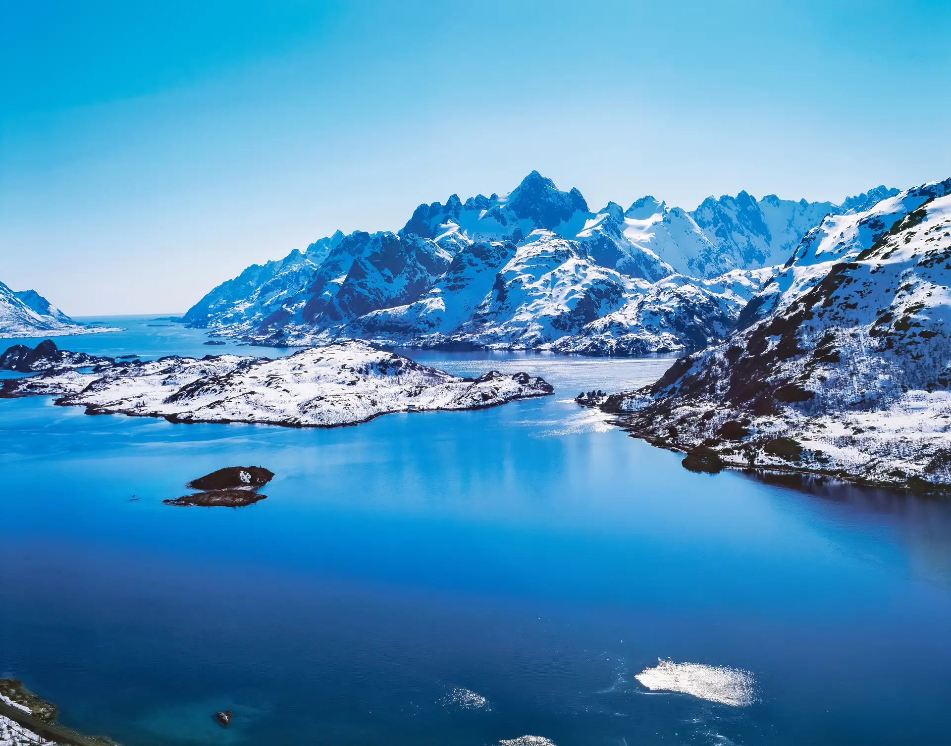 Eine friedliche Winterlandschaft mit schneebedeckten Bergen, die sich in einem leuchtend blauen See unter klarem Himmel spiegeln. Die Szene strahlt Ruhe und Erhabenheit aus.