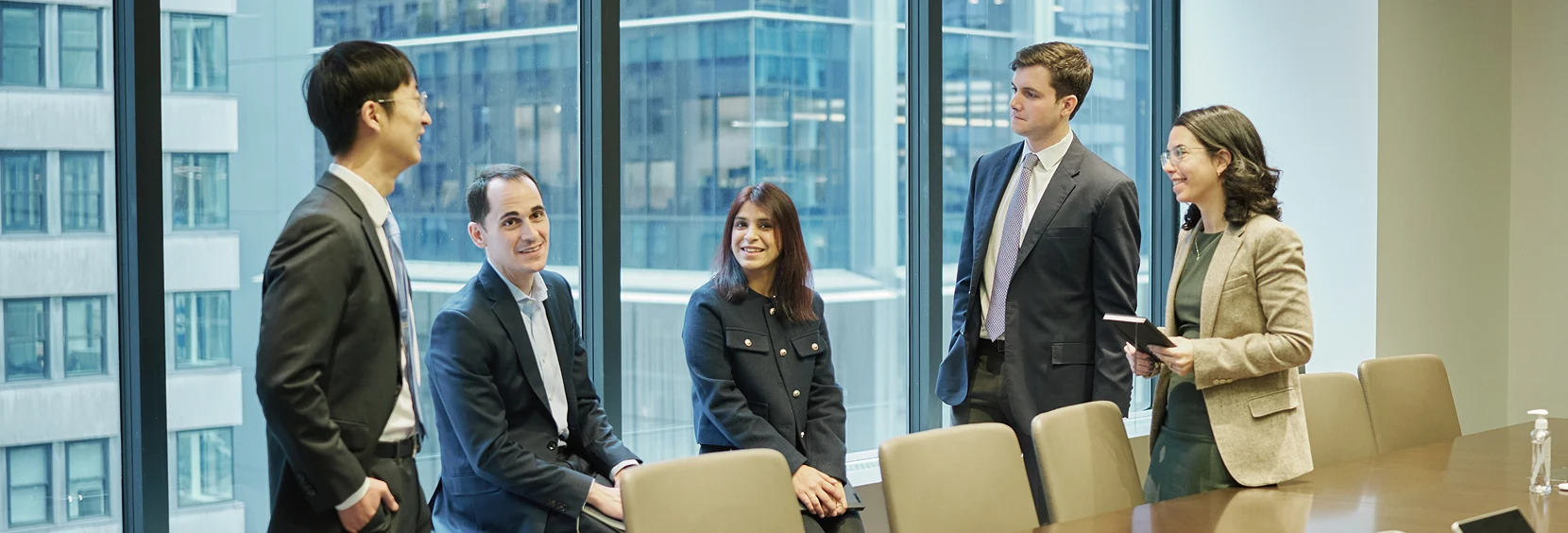 Five people in a board room talking in front of a wall of windows