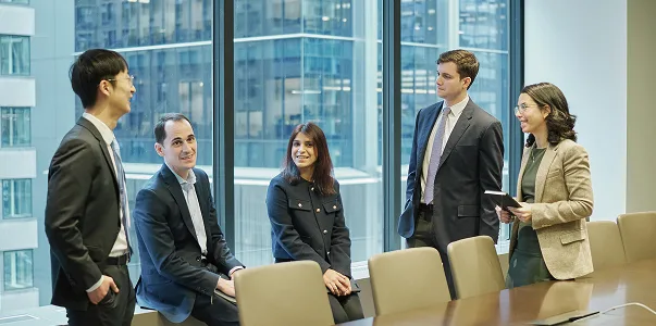 Five people in a board room talking in front of a wall of windows