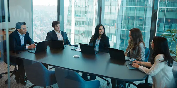 Five people in a board room talking in front of a wall of windows