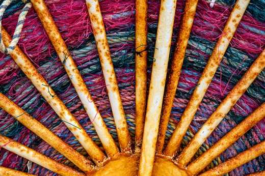 Photograph of brightly colored fishing nets winded up onto a heavily corroded wheel for storage.