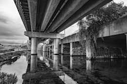 Black and white photograph of the reflections of a concrete overpass strewn with graffiti, an abandoned and forgotten space.
