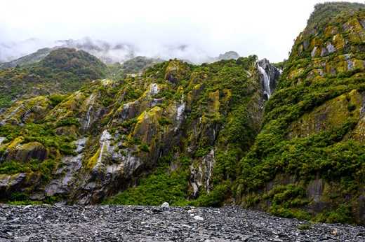 Photograph of waterfall making its way down a steep rock face covered in lush vegetation.