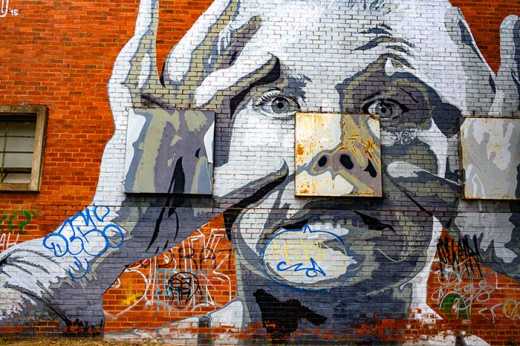 Photograph of street art depicting a person holding their eyes wide open with their fingers. 