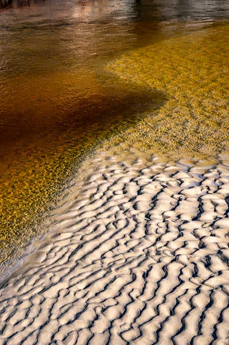 Photograph of the patterns and colors created by the flow of a tea tree stained river and sand.