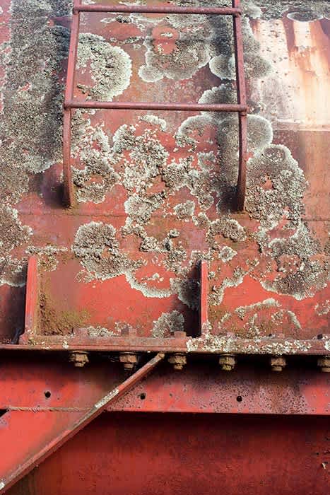 Photograph of a ladder on the side of an old rusty tank.