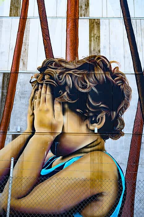 Photograph of large scale street art depicting a small child hiding their face in their hands.