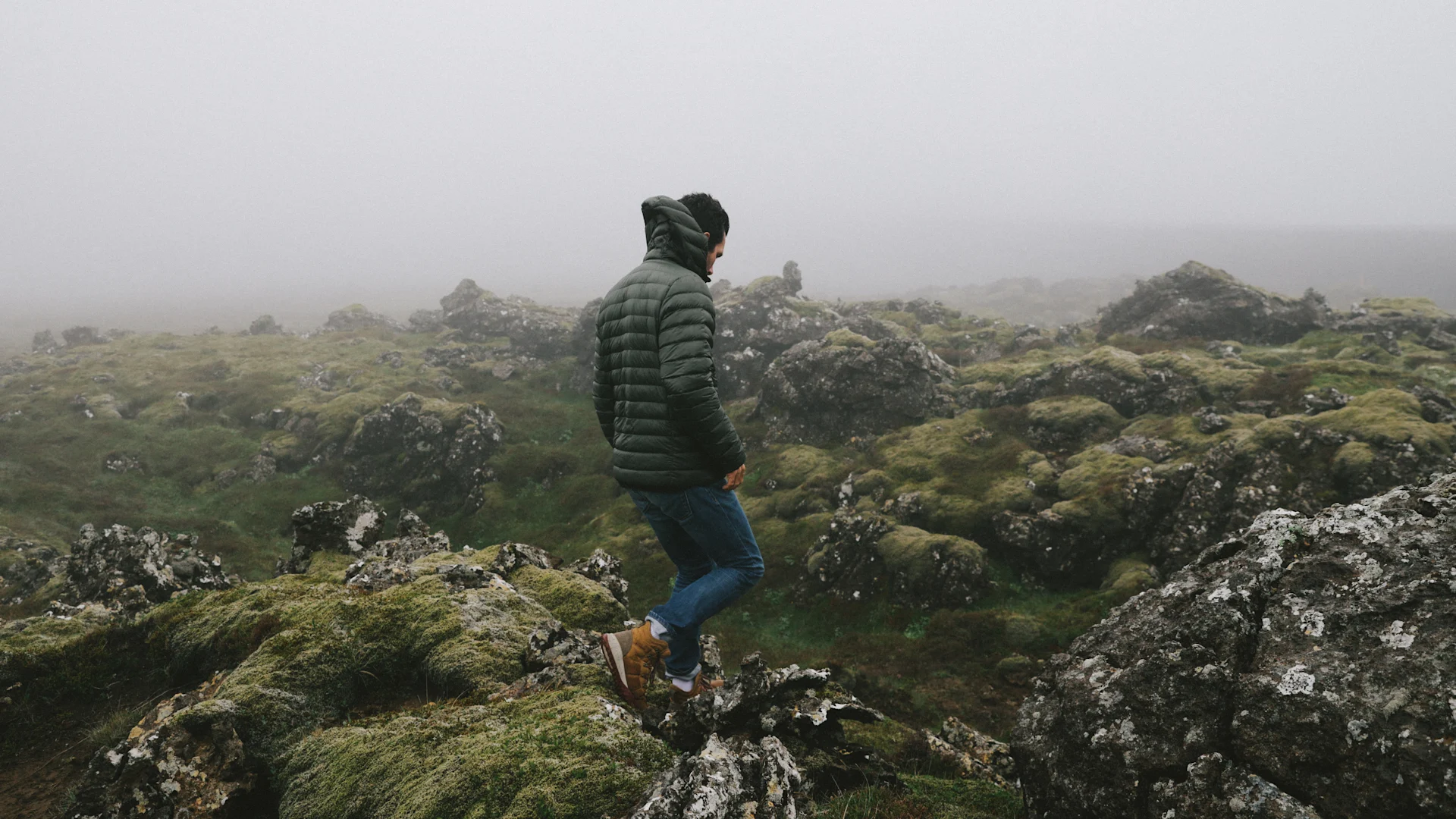a travel photo of a man walking through a mossy rocky terrain