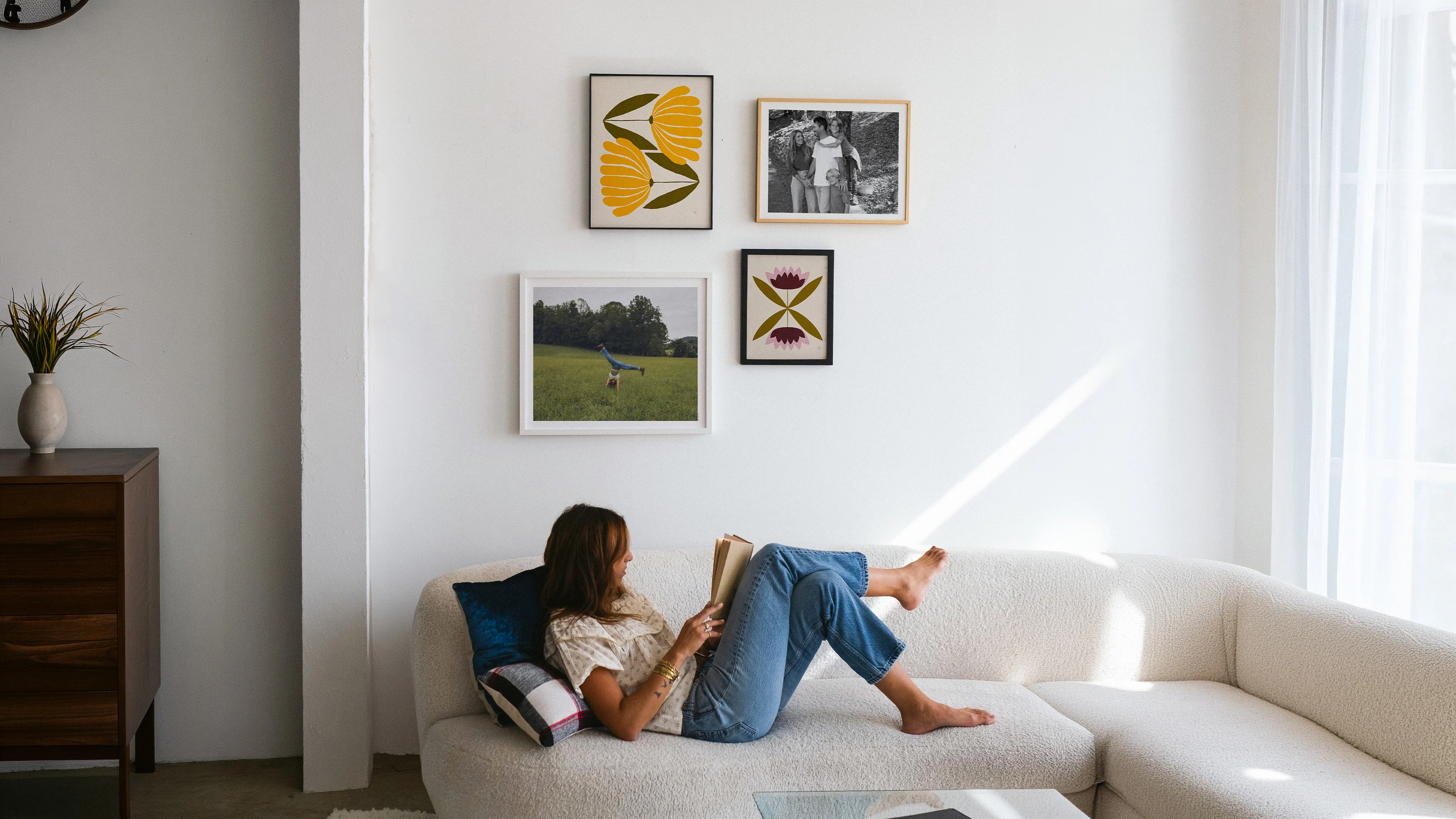 Gallery wall of Still Novel birth month flower prints for the months of November and July, framed beside family photos above a cream sofa.
