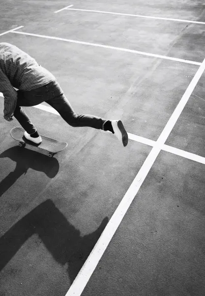 A black-and-white photograph of a skateboarder crossing a lined outdoor court.